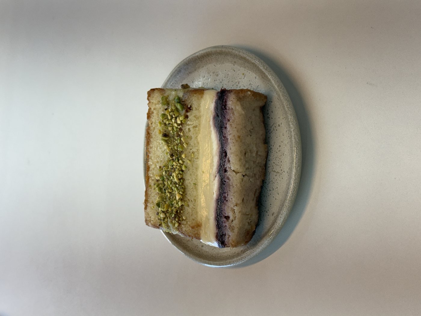 Fatia de bolo de pistache com recheio de creme e geleia de frutas vermelhas