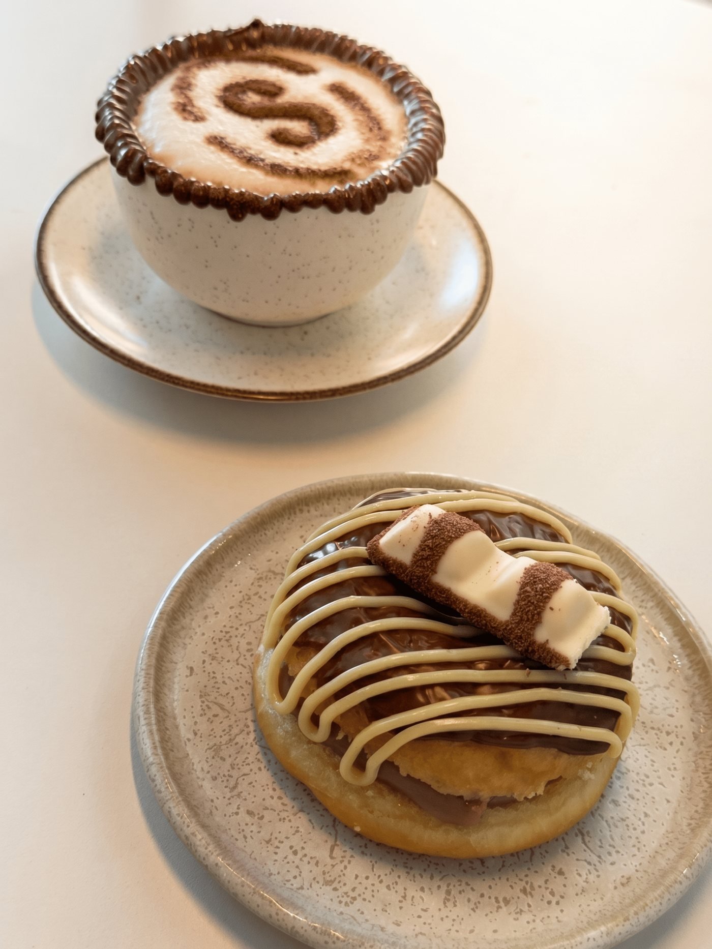 Cappuccino da Sapore Moretti com desenho em cacau, ao lado de uma sobremesa